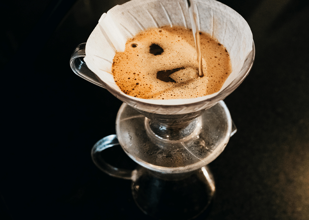 Close-Up Of A Pour-Over Coffee Setup With Hot Water Streaming Over Ground Beans In A Paper Filter. 